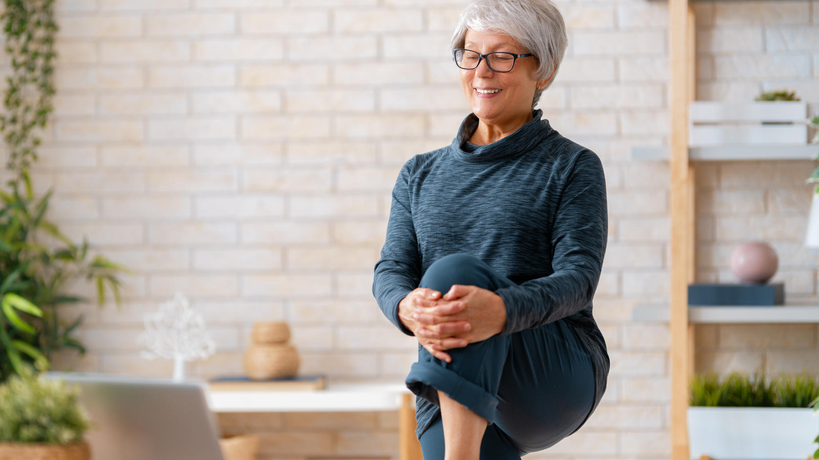 Senior woman in activewear watching online courses on laptop while exercising at home.