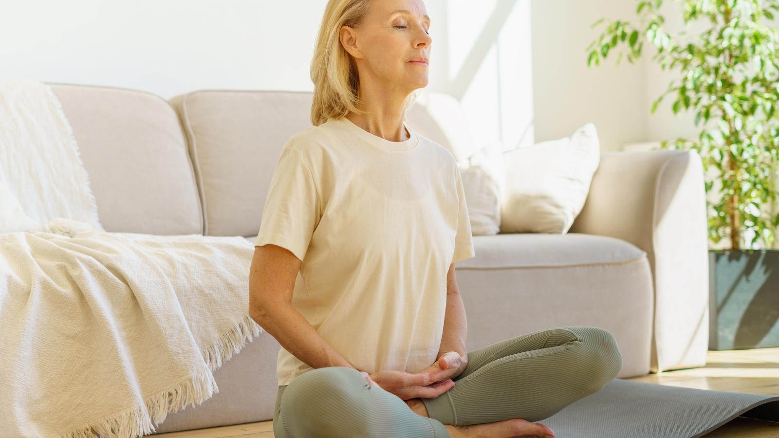 Calm elderly woman practicing meditation techniques and yoga. Peaceful senior woman in lotus position meditation with closed eyes at home practicing yoga.