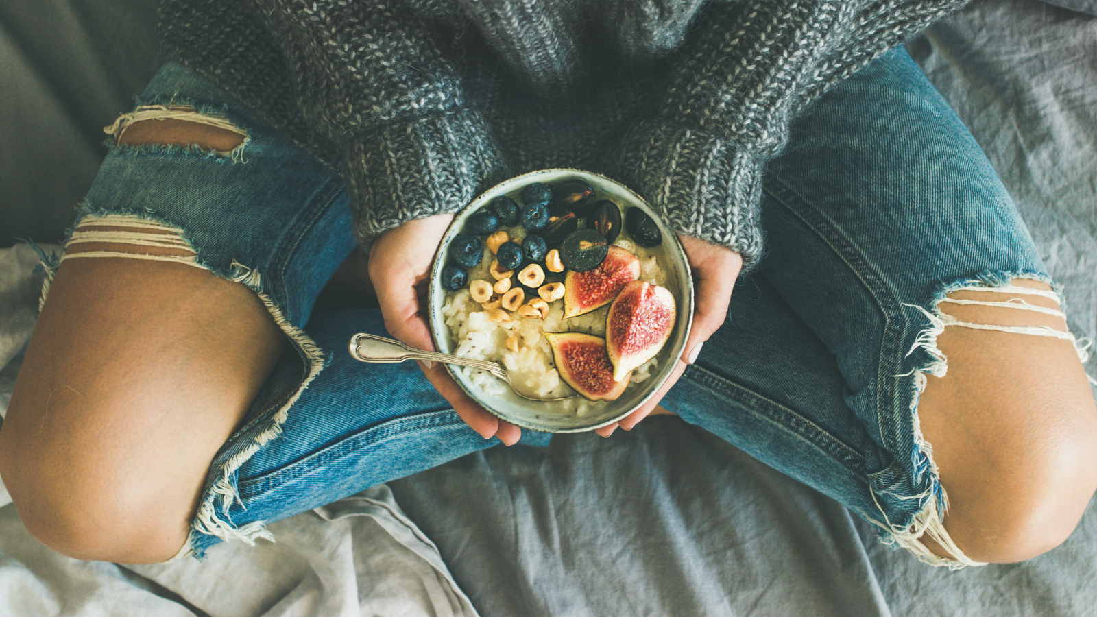 Yoga can help with mindful and healthy eating habits Healthy winter breakfast in bed. Woman in sweater and jeans holding rice coconut porridge with figs, berries, hazelnuts to enhance heart health