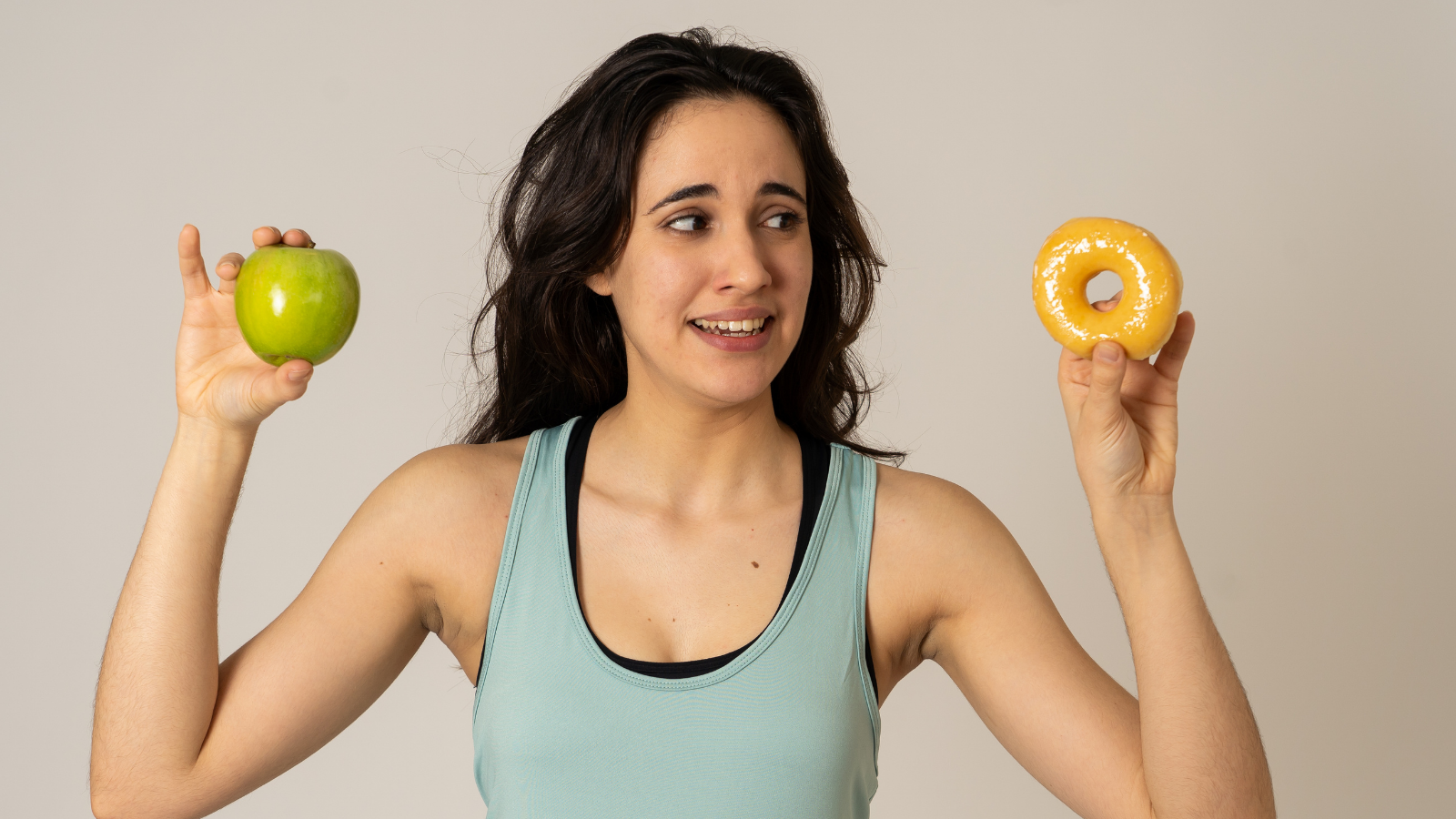 Fitness and nutrition healthy lifestyle for optimum performance in running Beautiful young fit woman tempted having to make choice; apple and doughnut, healthy or unhealthy food