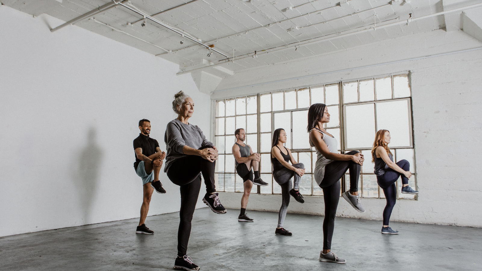 How to practice balance to improve overall health and arthritis symptoms older woman among diverse people stretching their knees and practicing balance in a yoga class to help relieve arthritis pain